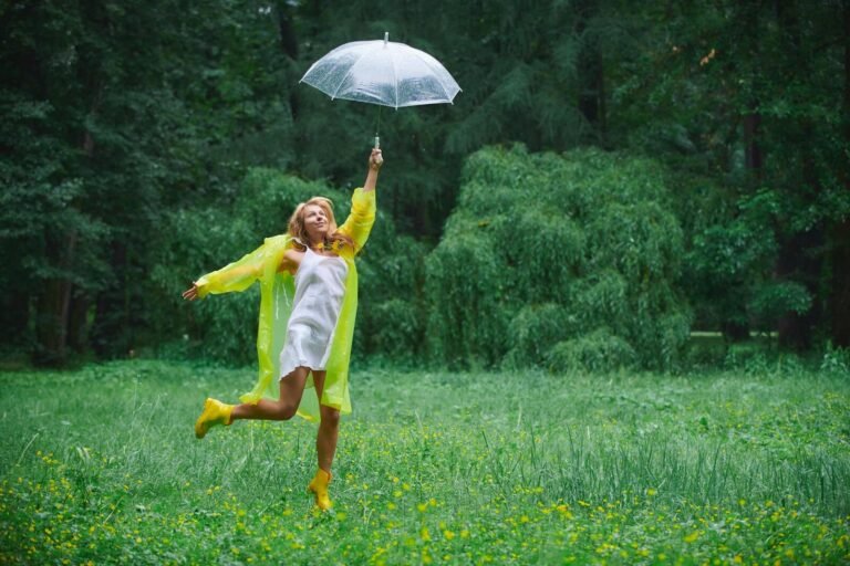 Cheerful woman jumping with an umbrella on a rainy day in a lush green park.
