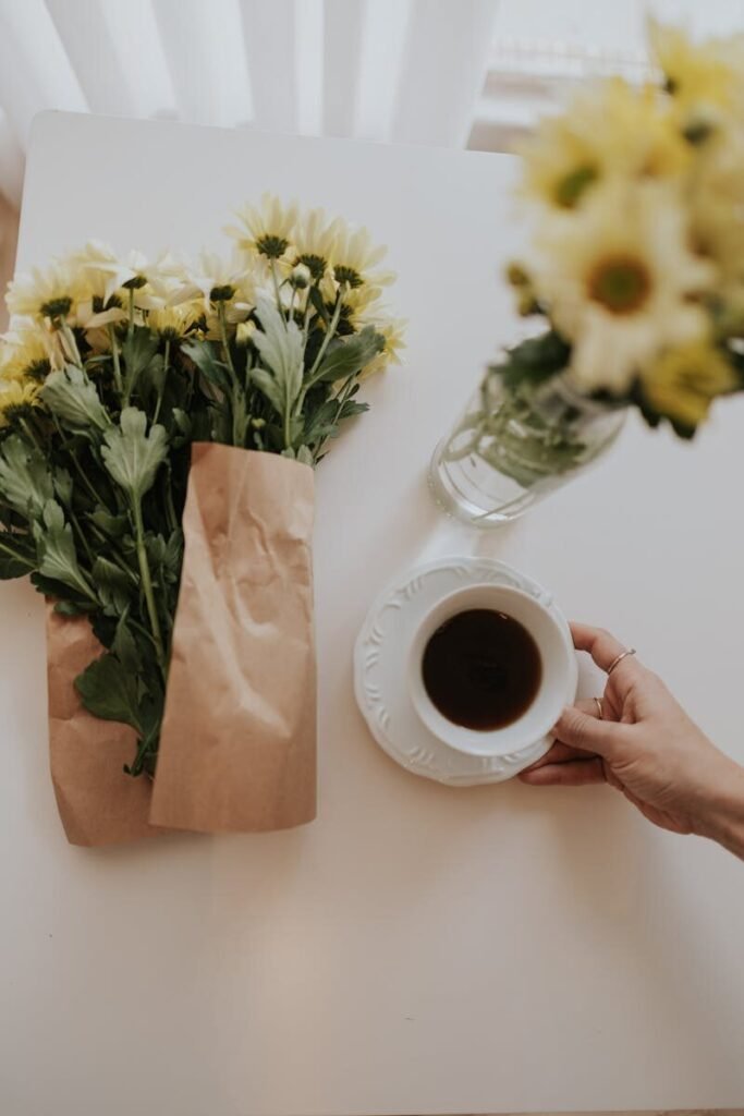 Flat lay of a coffee cup, yellow daisies, and brown paper on a white table.