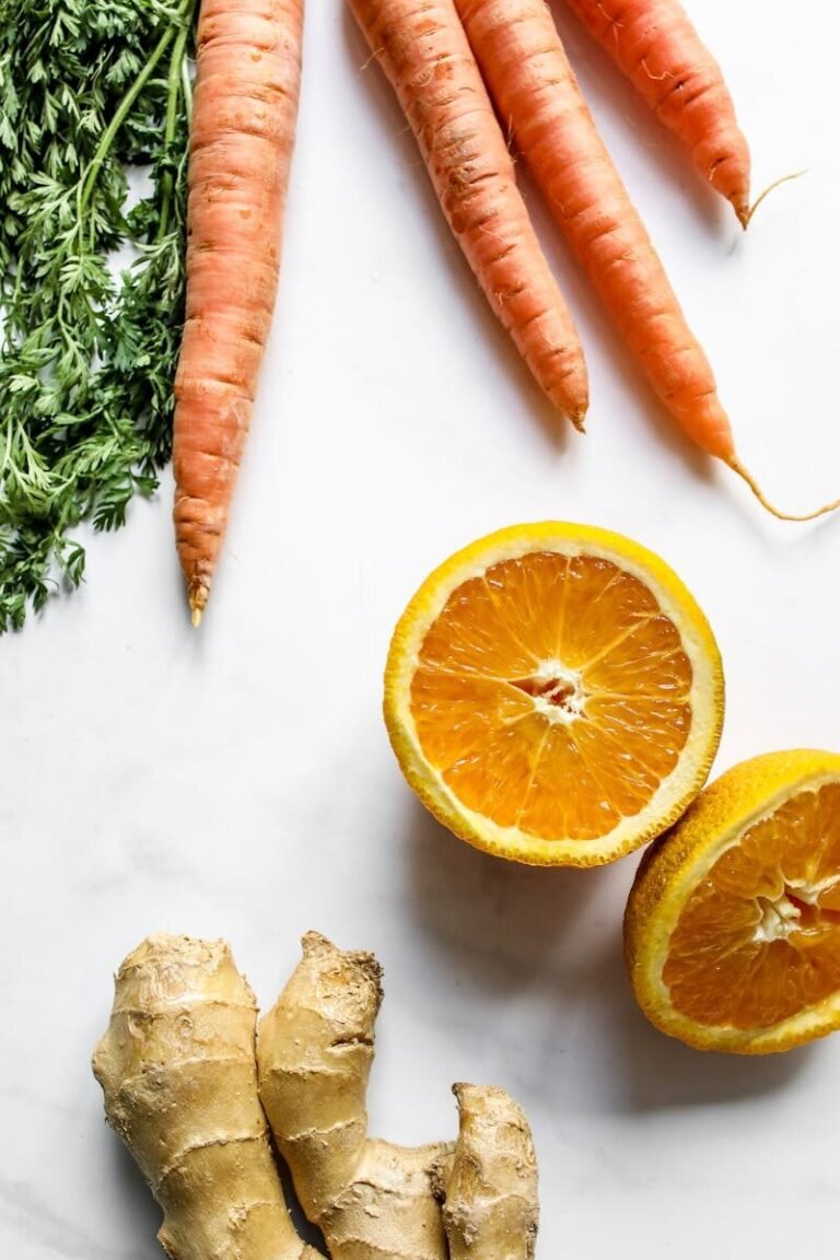 Fresh carrots, oranges, and ginger arranged on a white surface viewed from above.