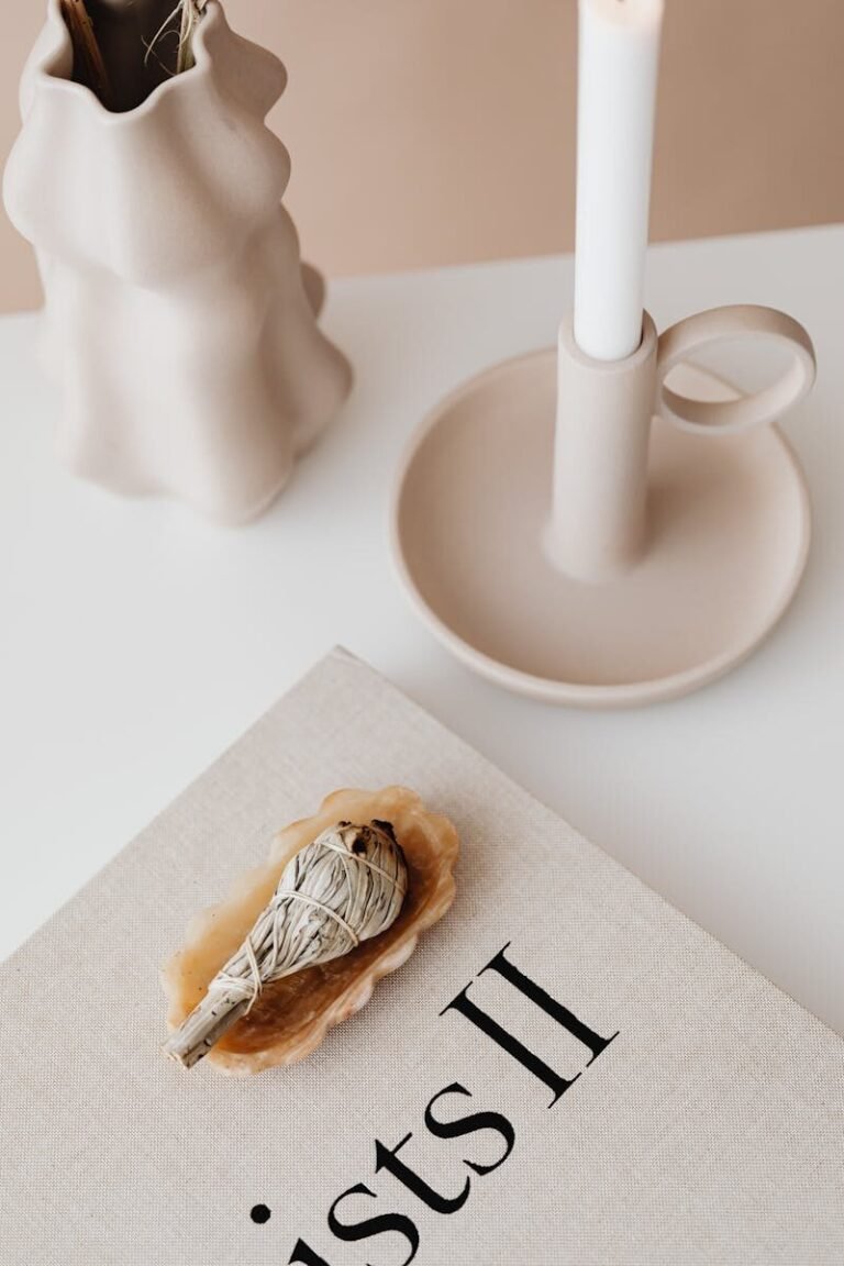 Elegant minimalist setup featuring a book, candle, and vase on a white table.