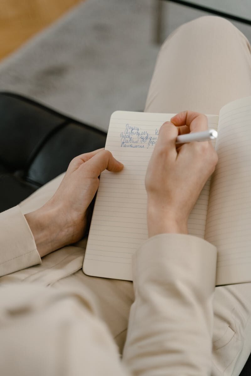 Close-up of an adult writing in a notebook with a pen indoors.