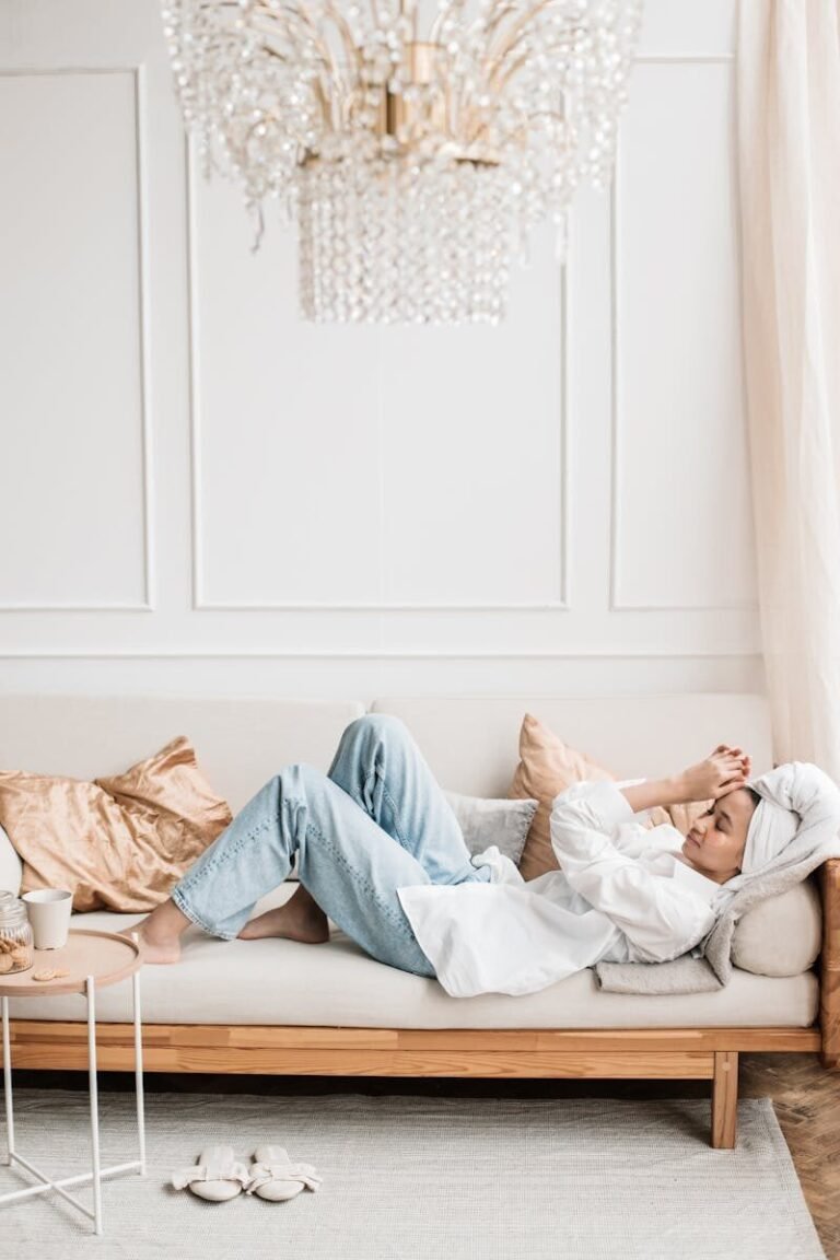 A relaxed woman with towel on head lies on a stylish sofa under chandelier, enjoying leisure time.