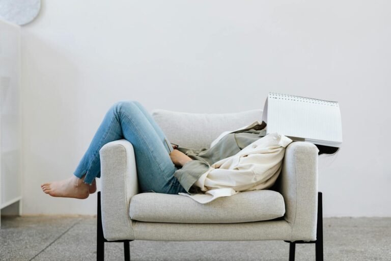 Woman lounging indoors on a chair with a notebook covering her face, depicting relaxation.