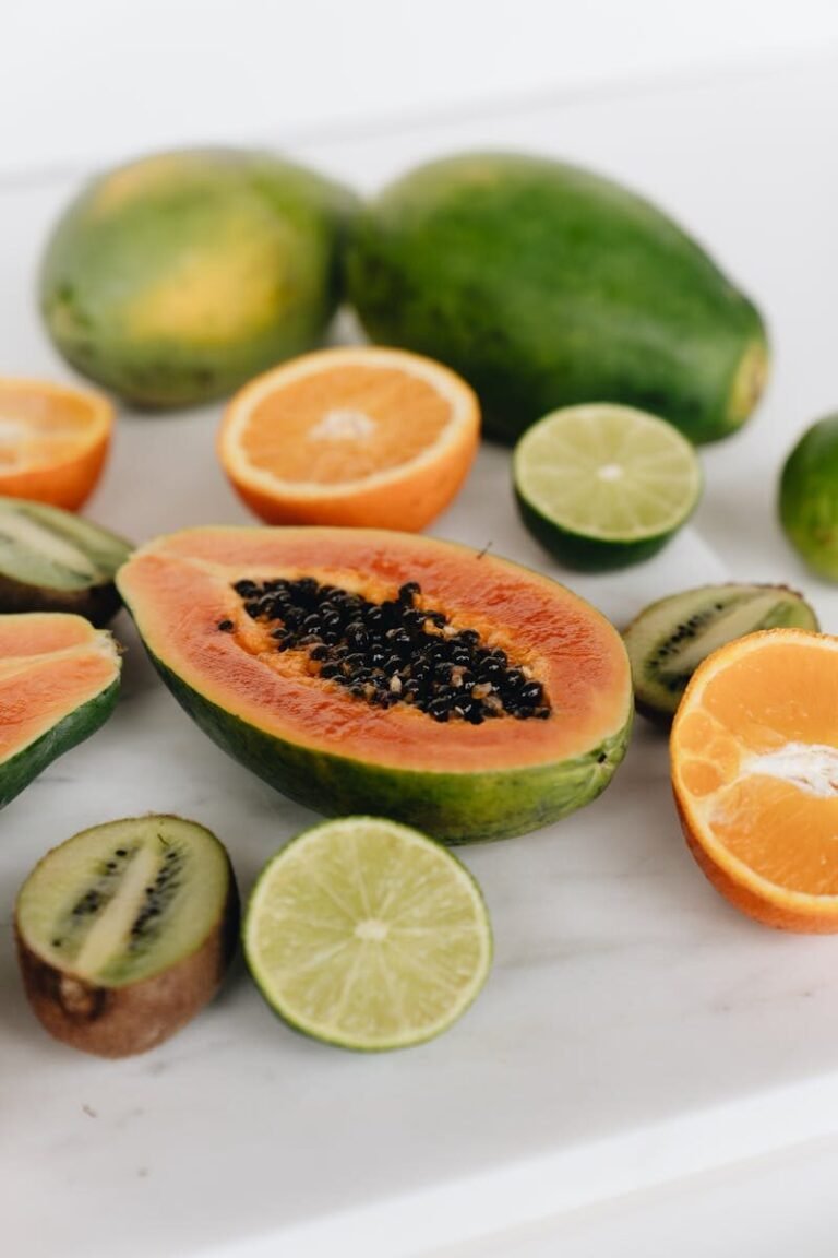 A vibrant arrangement of sliced tropical fruits, including papaya, oranges, limes, and kiwi, on a white surface.
