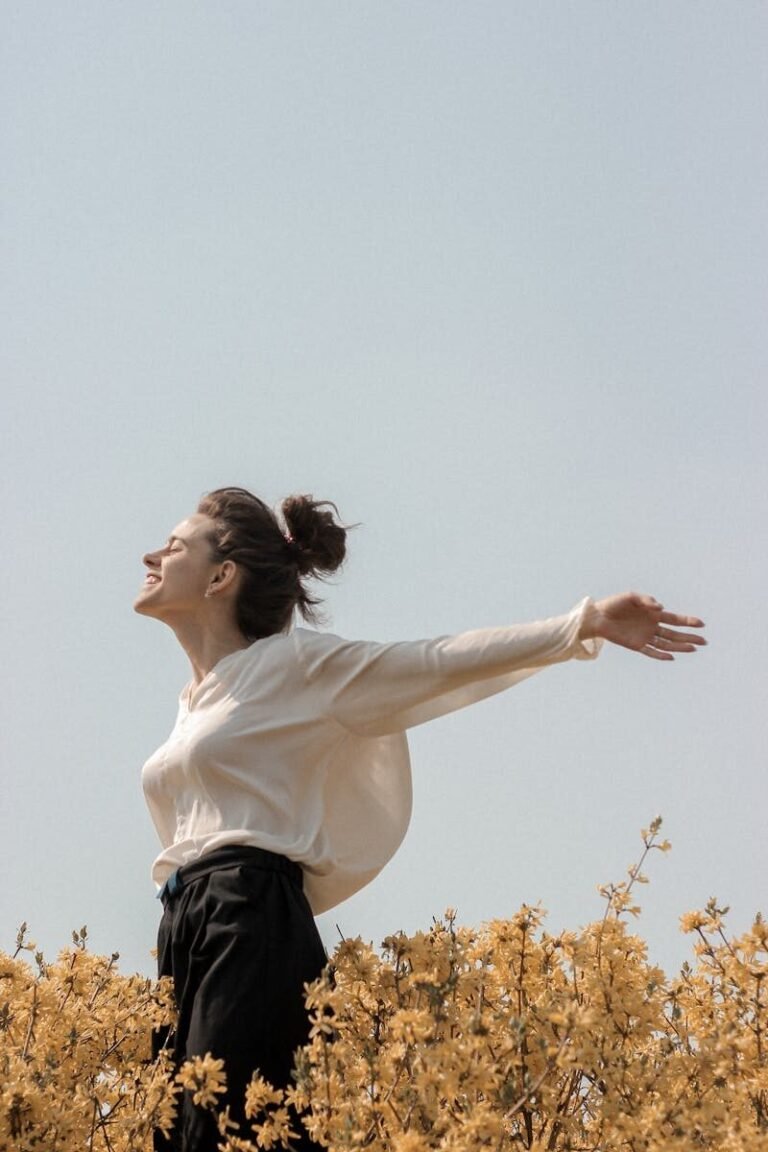 A woman in a white blouse enjoys the outdoors in a springtime field of yellow flowers.