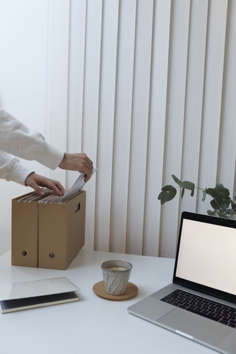Crop anonymous person folding documents while working in contemporary office with laptop and coffee