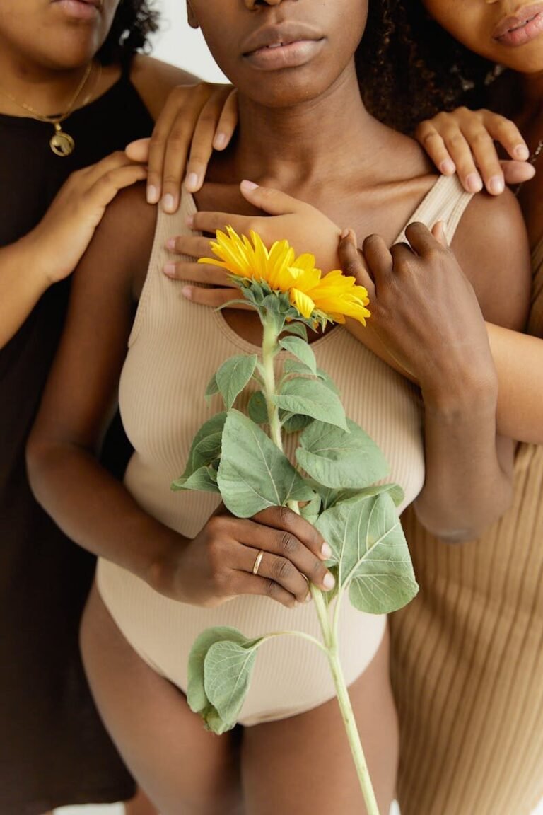 A close-up of diverse women in leotards embracing with a sunflower, highlighting unity and femininity.
